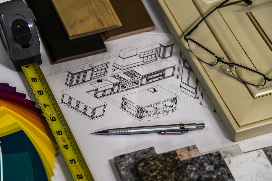kitchen remodeling plans surrounded by measuring tape, a cabinet sample, glasses, a mechanical pencil, countertop samples, measuring tape, wood samples, and color samples