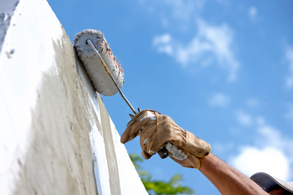 builder worker painting facade of high-rise building with roller