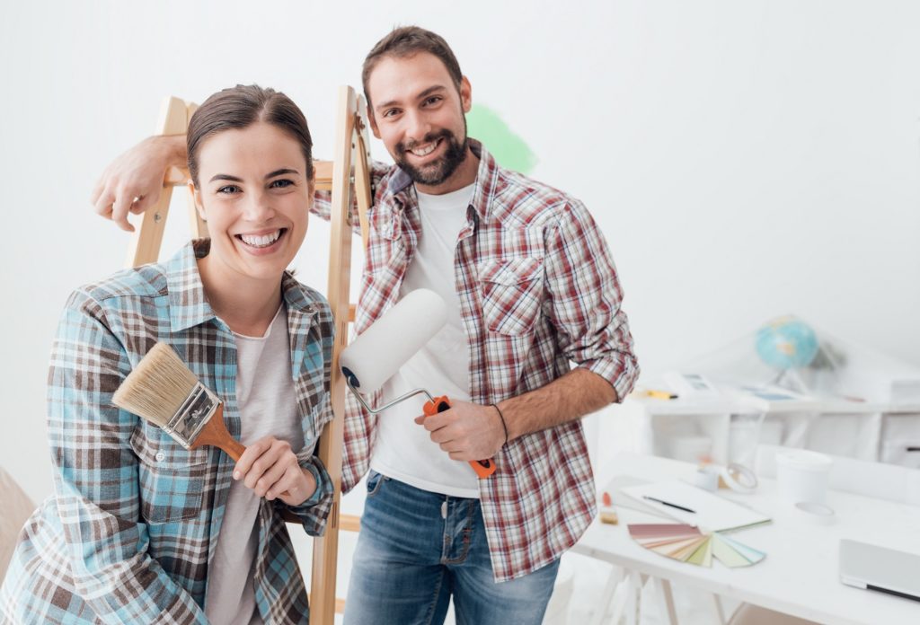 Creative young couple remodeling their house and painting walls, they are posing together and smiling at camera