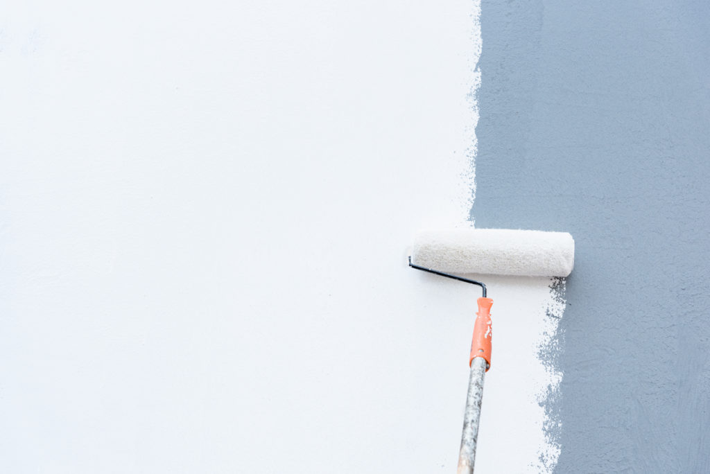 Roller brush applies a fresh coat of white paint over a light blue wall surface.